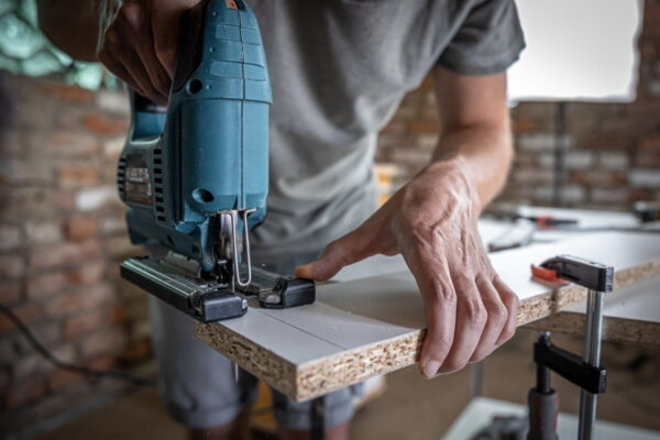 A male carpenter cuts a wood with an electric jigsaw, working with a tree.